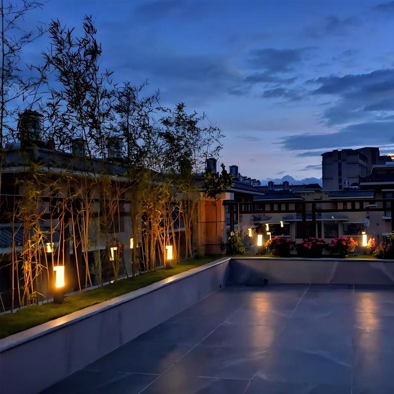 Modern rooftop garden with bamboo plants and LED bollard lights illuminating the space at dusk, showcasing elegant landscape lighting design