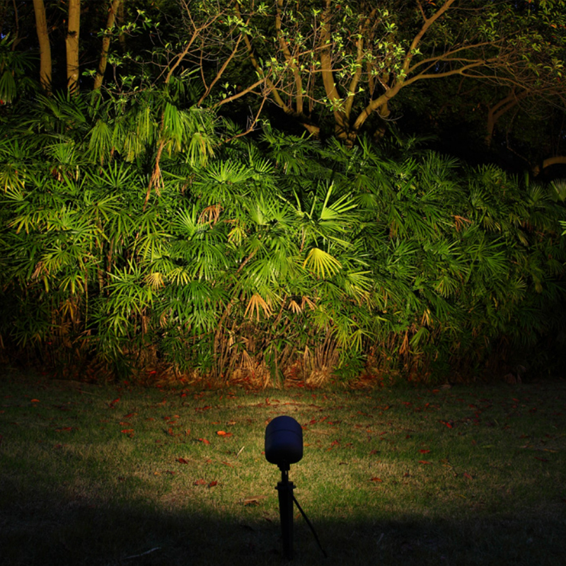Outdoor LED spotlight illuminating dense green foliage and trees in a landscaped garden at night, showing effective garden lighting design