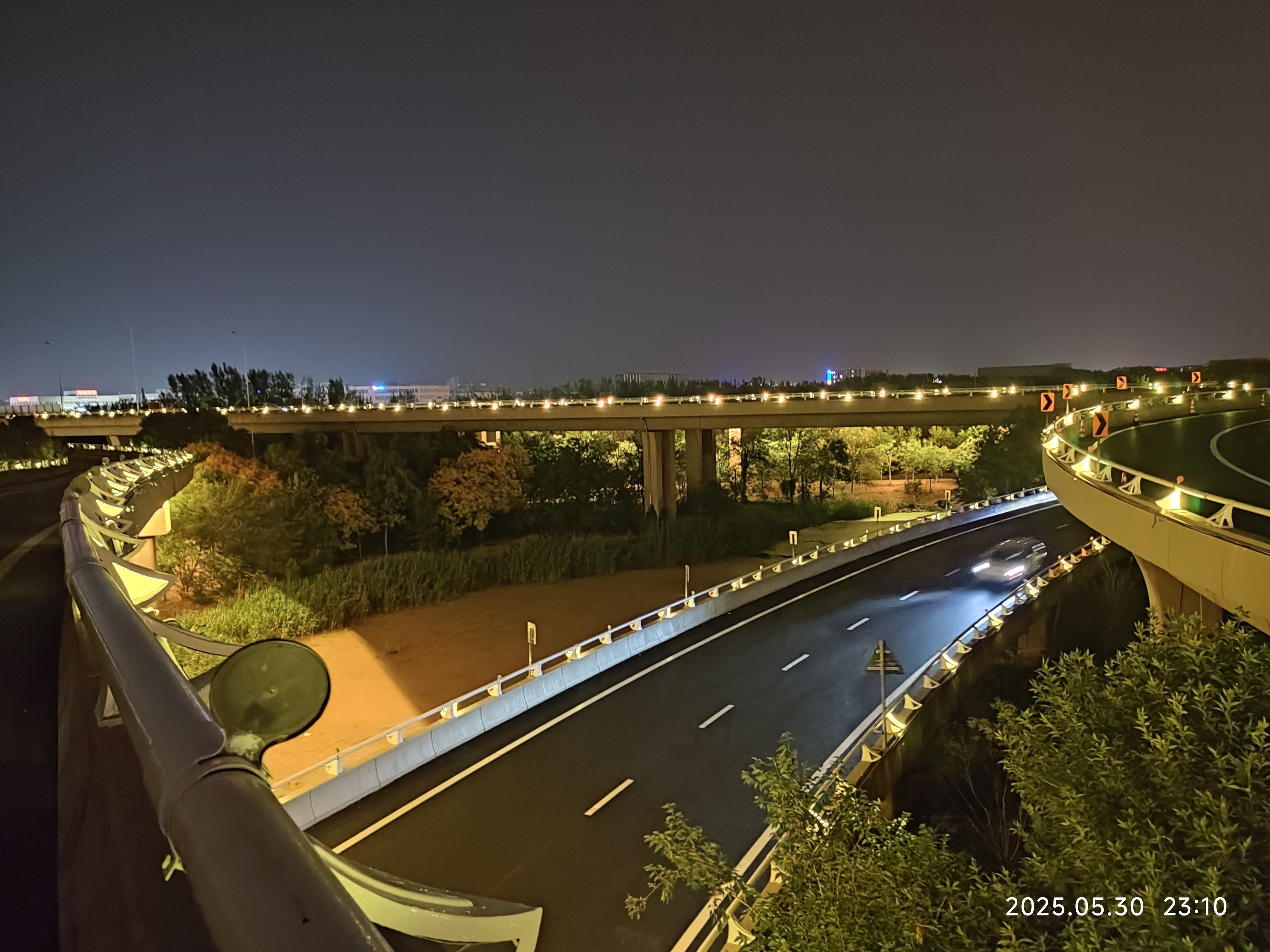 Elevated spiral highway ramp at night, showing road curves, greenery and a timestamp — façade lighting, infrastructure lighting, bridge and roadway illumination, exterior LED lighting, structural façade lighting
