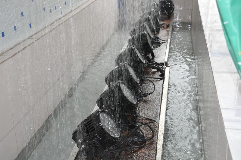 A row of LED flood lights undergoing a high-pressure water spray test to demonstrate their IP66 waterproof rating and outdoor durability.