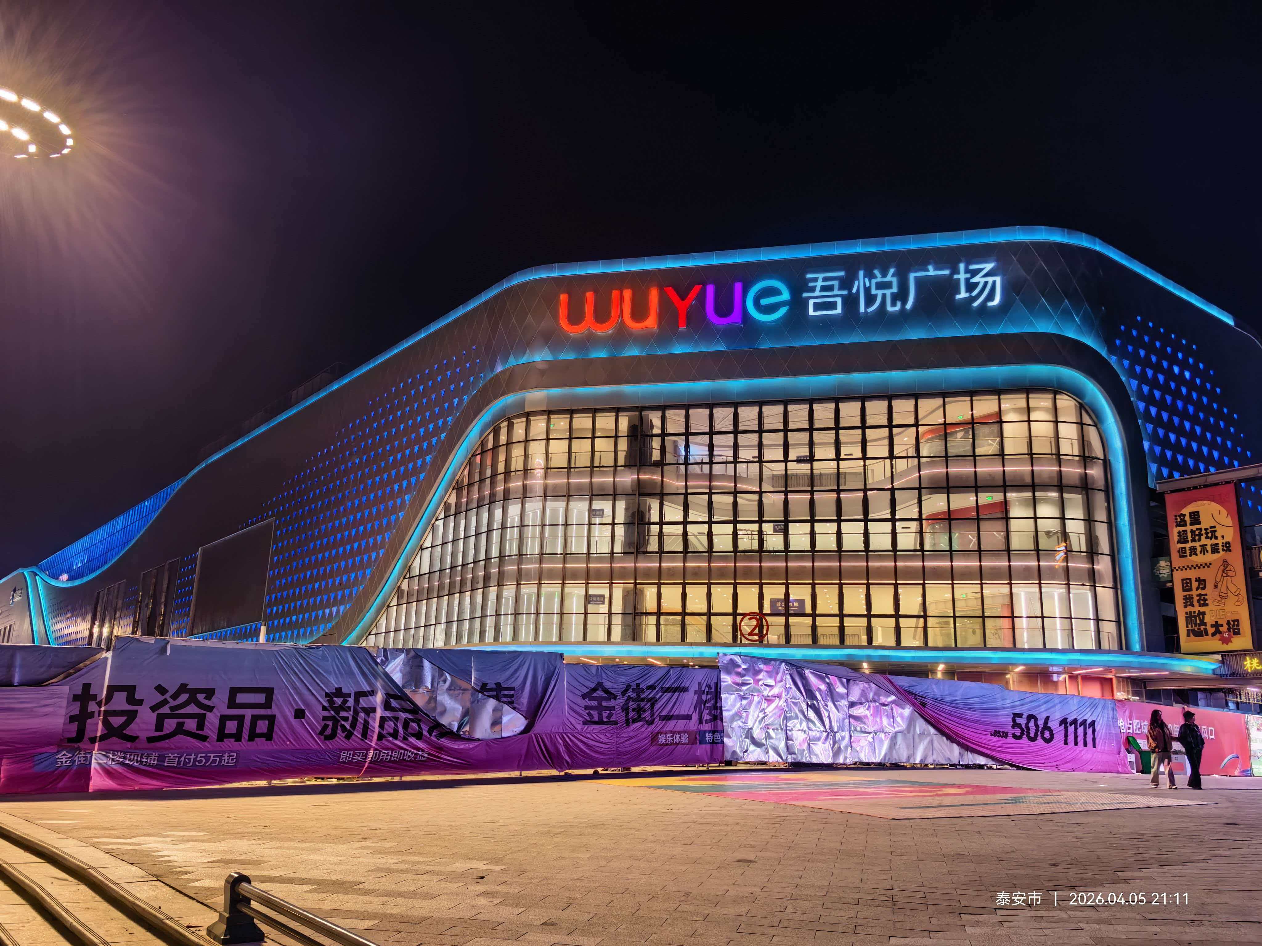 Feicheng Wuyue Plaza main entrance featuring LNJAMI colorful brand signage and architectural facade lighting at night.