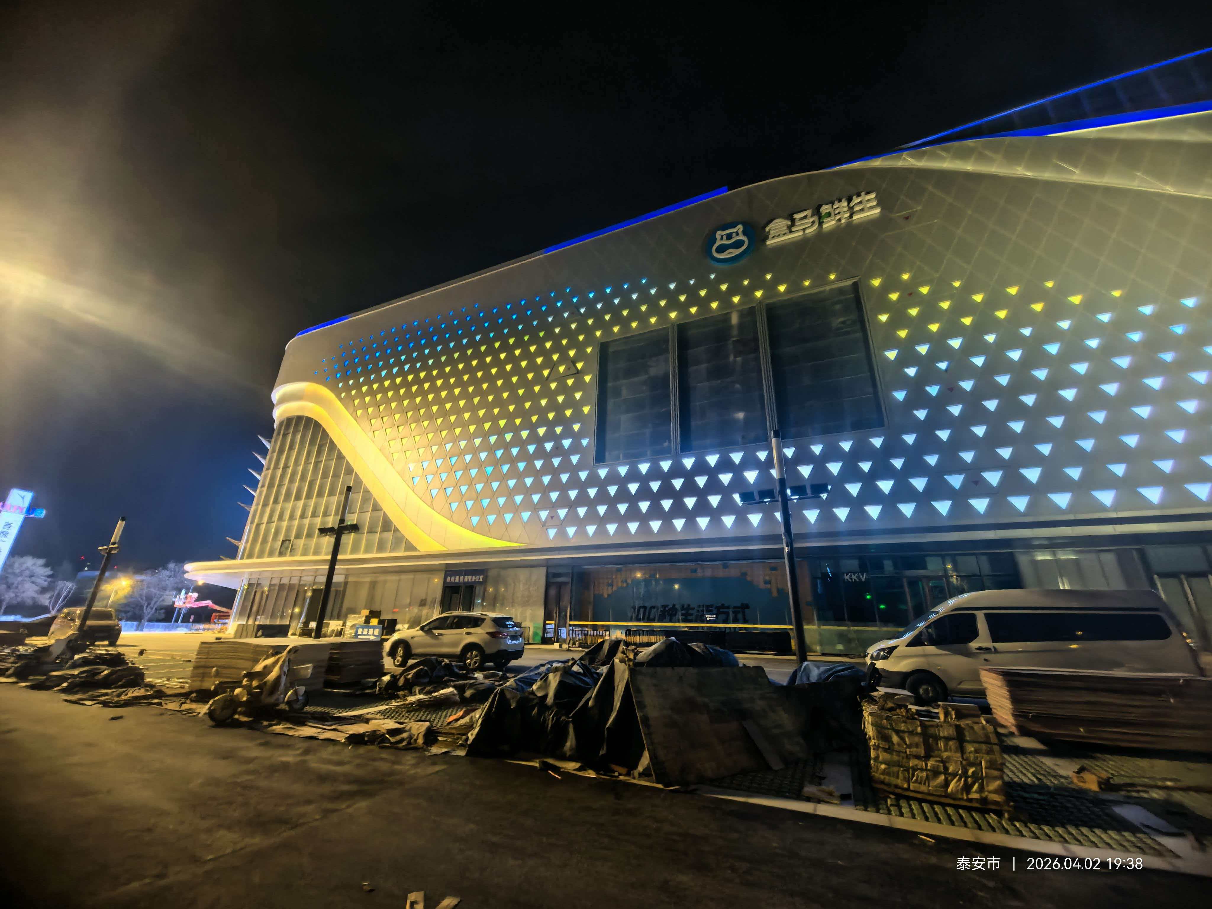 Custom triangular light guide panels and blue LED facade texture on Feicheng Wuyue Plaza with Hema Fresh logo.
