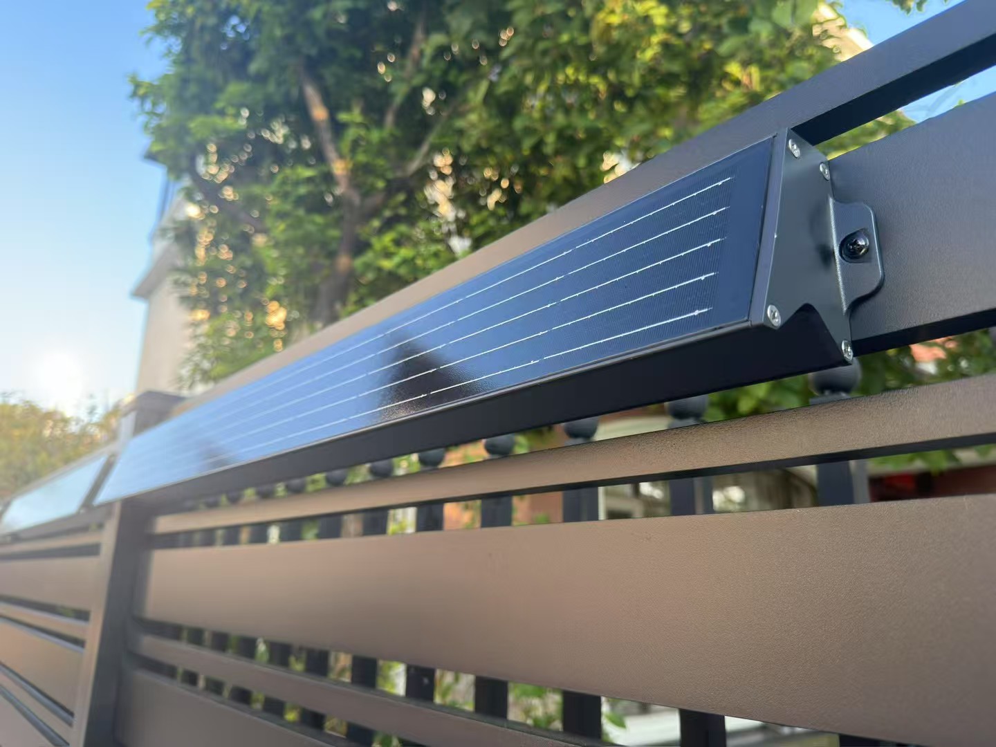 Close-up detail of compact solar wall washer luminaire mounted on outdoor metal fence for cable-free installation.