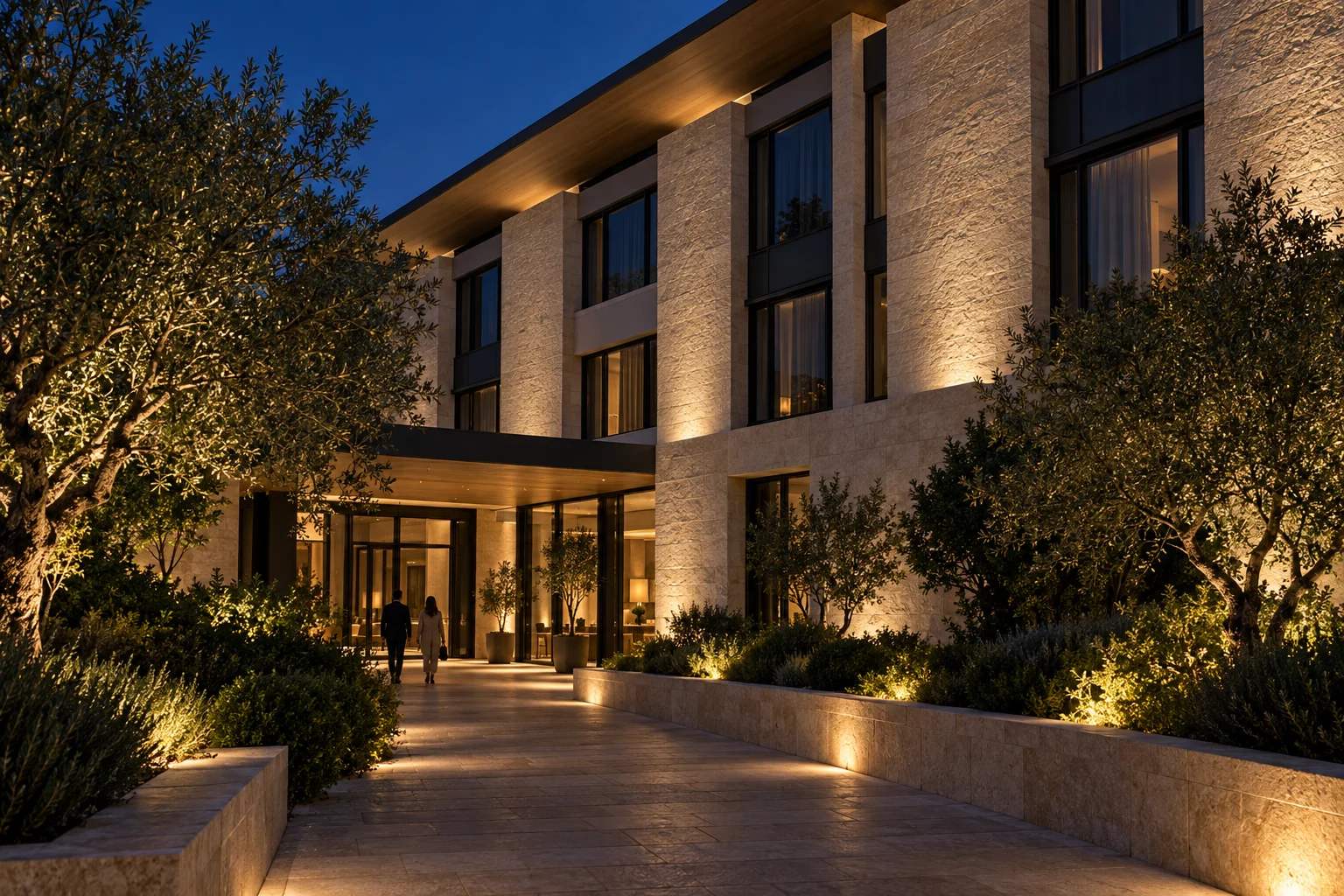 Pedestrian approach to a stone hotel facade with warm wall washing and recessed windows